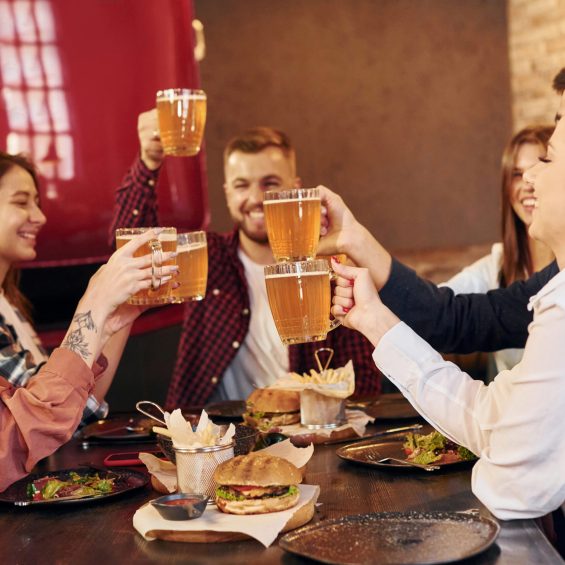 Having a conversation with each other. Group of young friends sitting together in bar with beer.